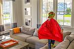 Boy with red cape playing on sofa