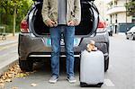 Mid adult man standing beside car with open boot, suitcase in road