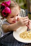 High angle vew of girl with pink hair bow sitting at garden eating spaghetti