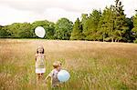 Brother and sister in tall grass playing with balloon