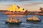 The Passenger ferries, the Scarborough and Friendship pass in front of the Sydney Opera House, Bennelong Point, at sunset, viewed from the Rocks, Sydney, New South Wales, Australia.
