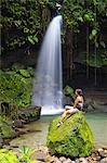 Dominica, Castle Bruce. A tourst sits on a rock at Emerald Pool. .