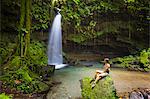 Dominica, Castle Bruce. A tourst sits on a rock at Emerald Pool. .