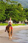 Dominica, Portsmouth. A young woman rides a horse on Purple Turtle Beach. .