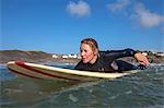 UK, Cornwall, Polzeath. A woman paddles out in the waves off Polzeath beach.