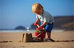 UK, Cornwall, Polzeath. A young boy puts the finishing touches to his sand castle.