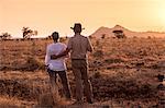 Kenya, Meru. A couple enjoy a sundowner, looking out towards a lone giraffe.