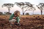 Kenya, Meru. A young boy plays with his safari toys in the dust in Meru National Park.