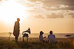 Kenya, Mara North Conservancy. A couple enjoy a sundowner in the Mara, listening to music from a vintage Gramophone.