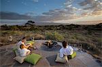 Kenya, Amboseli, Tortilis Camp. A young family sits at a fire pit overlooking Amboseli National Park, towards Kilimanjaro.