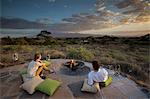 Kenya, Amboseli, Tortilis Camp. A young couple at the fire pit overlooking Amboseli National Park, towards Kilimanjaro.