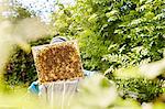 A beekeeper holding up and checking a honeycomb frame from a beehive.