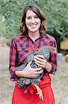 Portrait of a smiling woman holding a grey specked hen.