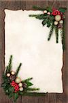 Christmas background floral border with gold bauble decorations, holly, ivy, fir and pine cones on parchment paper over old oak wood.