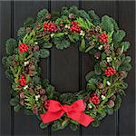 Christmas wreath with red bow, holly, mistletoe and winter greenery over dark blue oak front door background.