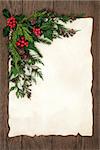 Christmas background border with holly, ivy, fir and cedar cypress  on parchment paper over old oak wood.