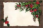 Christmas background floral border with red bauble decorations, holly, ivy, fir, cedar cypress and pine cones on parchment paper over old oak wood.