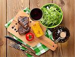 Steak with grilled corn, salad and red wine on wooden table. Top view