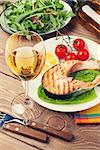 Grilled salmon and whtie wine on wooden table. Toned
