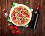 Italian pizza with pepperoni, tomatoes, olives, basil and red wine on wooden table. Top view