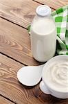 Sour cream in a bowl and milk bottle on wooden table with copy space