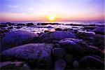 Pebble beach with ocean waves on sunset.