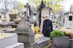 Solitary woman mourning by gravestone, remembering dead relatives in on Pere Lachaise cemetery in Paris, France.