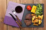 Steak with grilled potato, corn, salad and red wine on wooden table. Top view