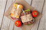 Two sandwiches with salad, ham, cheese and tomatoes on wooden table. Top view