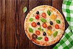 Italian pizza with cheese, tomatoes, olives and basil on wooden table. Top view with copy space
