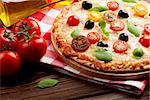 Italian pizza with cheese, tomatoes, olives and basil on wooden table