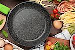 Pasta cooking ingredients and utensils on wooden table. Top view with empty frying pan for copy space