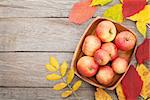 Apples in bowl and colorful autumn leaves on woden background with copy space