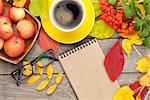 Autumn leaves, apple fruits, coffee cup and notepad for copy space over wood background