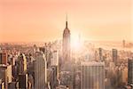 New York City. Manhattan downtown skyline with illuminated Empire State Building and skyscrapers at sunset. Horizontal composition. Warm evening colors. Sunbeams and lens flare.