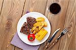 Steak with grilled potato, corn and red wine on wooden table
