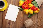 Colorful tulips bouquet, blank greeting card and coffee cup on wooden table