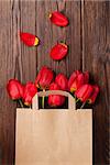 Red tulips bouquet in paper bag over wooden table background with copy space