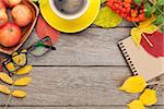 Autumn leaves, apple fruits, coffee cup and notepad over wood background with copy space