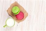 Colorful macarons and cup of milk on white wooden table with copy space