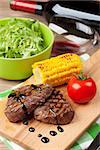 Steak with grilled corn, salad and red wine on wooden table