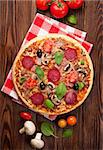 Italian pizza with pepperoni, tomatoes, olives and basil on wooden table. Top view