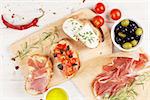 Bruschetta with cheese, tomatoes and prosciutto on cutting board