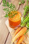 Fresh carrot juice smoothie and roots on wooden table