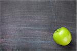 Green apple on blackboard or chalkboard background. Top view with copy space