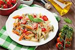 Colorful penne pasta with tomatoes and basil on wooden table