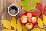 Autumn leaves, apple fruits and coffee cup over wood background