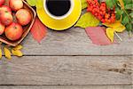 Autumn leaves, apple fruits and coffee cup over wood background with copy space
