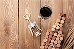 Wine bottle shaped corks, glass of wine and corkscrew over rustic wooden table background. View from above with copy space