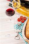 White and red wine, cheese and bread on white wooden table background. Top view with copy space